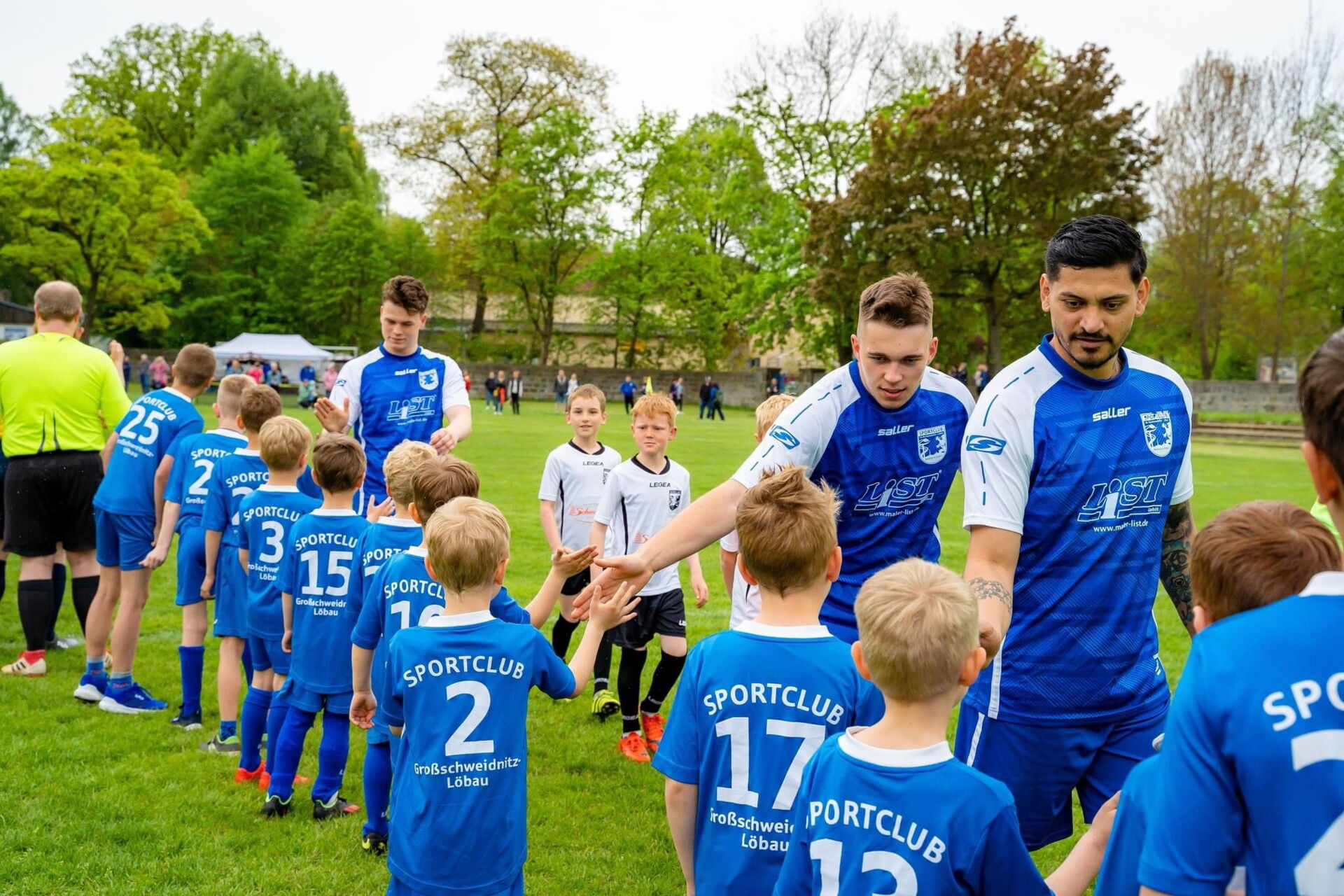 Spieler des Sportclub Großschweidnitz - Löbau e.V. klatschen mit Kindern auf dem Fußballfeld ab.