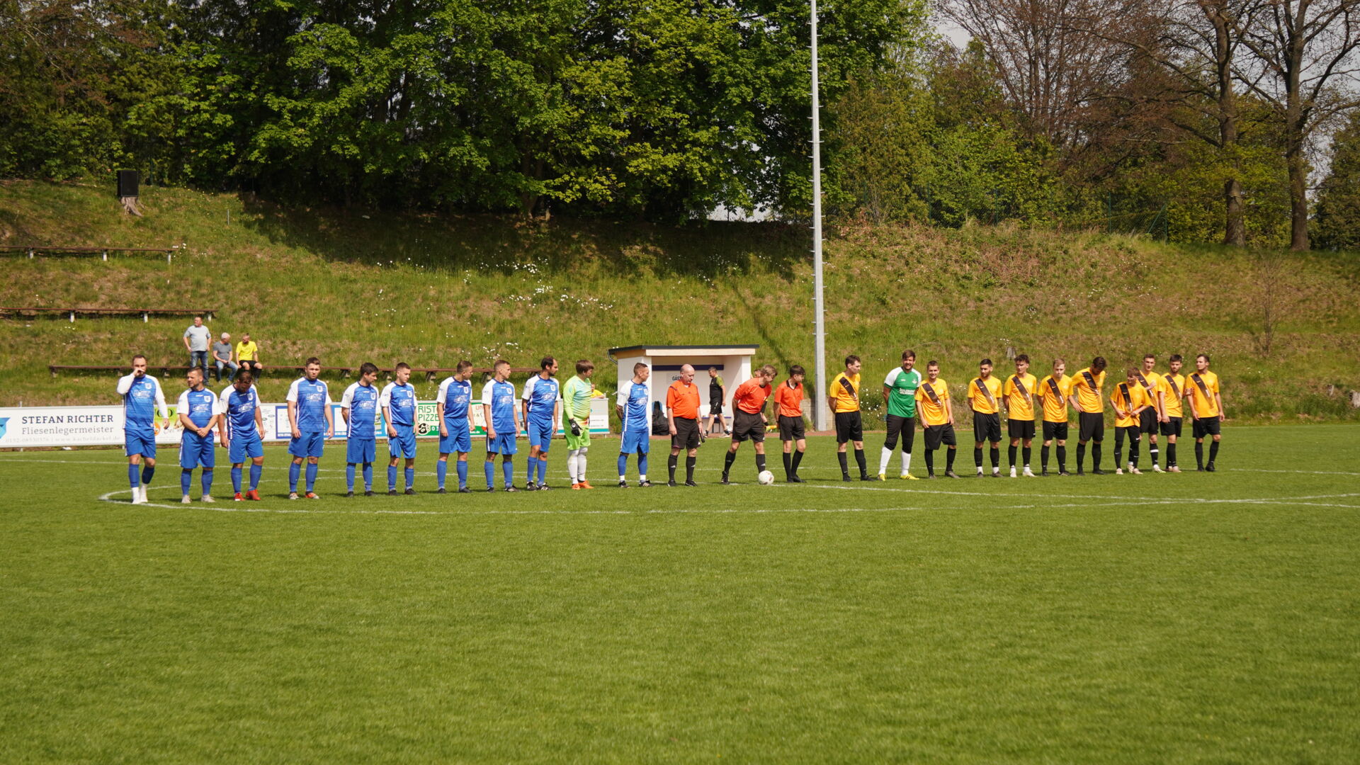 Zwei Fußballmannschaften, eine in Blau und eine in Gelb-Schwarz, stehen auf dem Spielfeld.